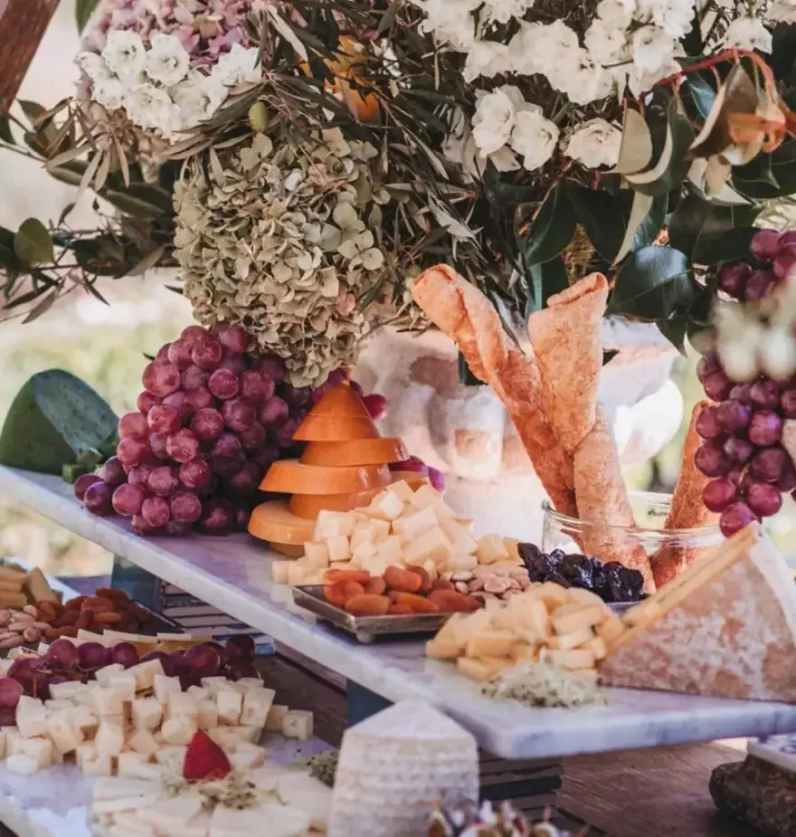 Mesa de bufé de boda con quesos, uvas, picos de pan, hortensias y flores blancas