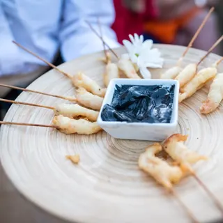 Bandeja de madera con brochetas de langostino y salsa negra en el cóctel