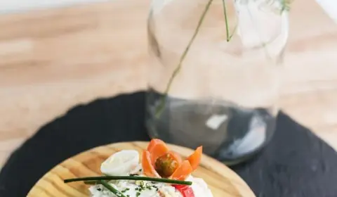 Ensaladilla rusa en forma de timbal sobre un plato de madera, con huevo de codorniz, pimiento rojo, zanahoria y cebollino