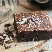 Porción de brownie de chocolate con virutas de chocolate blanco y negro sobre una rodaja de madera, del catering