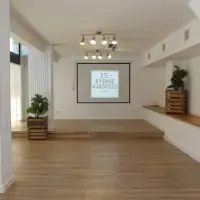 Sala diáfana de 25th Avenue Madrid con suelo de madera, columnas blancas, tarima y pantalla para presentaciones