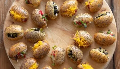 Tabla redonda de madera con mini brioche de amapola rellenos de huevo hilado, embutido y verduras para catering