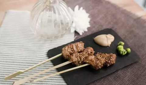 Tres brochetas de pollo yakitori con sésamo tostado, salsa cremosa y guisantes de wasabi sobre una pizarra