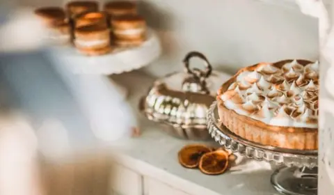 Tarta de limón con merengue tostado sobre un pie de cristal, con alfajores, una sopera de plata y naranja seca