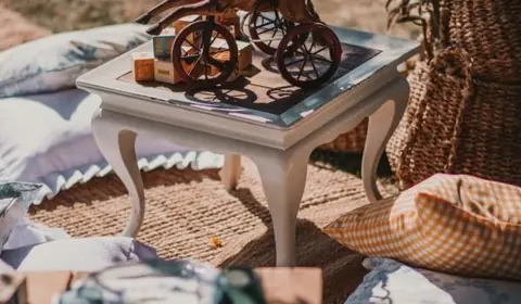 Caballito de madera sobre triciclo encima de una mesita blanca, con cojines, alfombras de fibra y cestos en un jardín