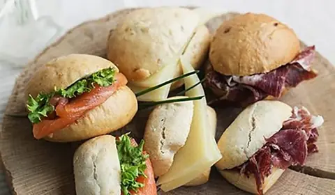 Pancitos rellenos de salmón ahumado con lechuga, de queso curado y de jamón ibérico sobre una gran rodaja de tronco