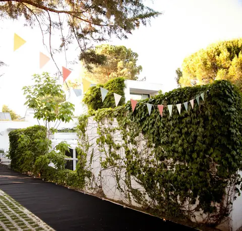 Entrada a una fiesta en una casa con muro de hiedra, banderines de colores y alfombra, preparada para recibir a los invitados