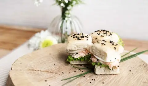 Panecillos tiernos con sésamo negro rellenos de una ensalada rosada, lechuga y cebolla sobre una rodaja de tronco