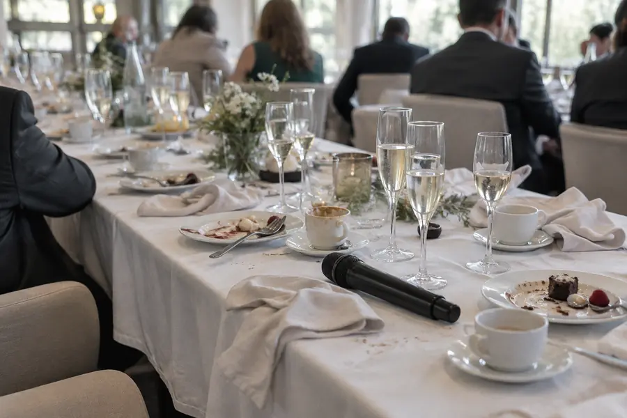 Mesa de cena de empresa tras el postre con copas de cava y un micrófono preparado para el discurso
