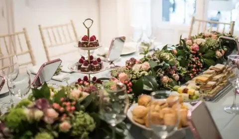 Mesa alargada con mantel azul claro, guirnaldas de flores, soportes de pisos con dulces de frambuesa y espejos rosas
