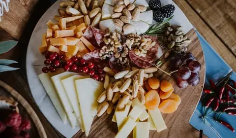 Tabla redonda con quesos en cuña y bastones, salami, almendras, nueces, orejones, uvas, moras y pistachos