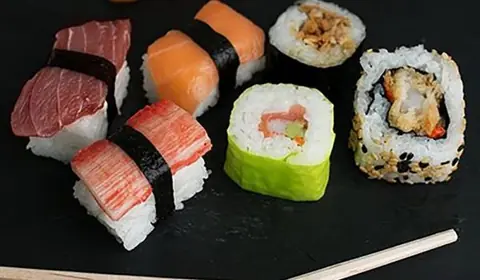 Niguiris de atún, salmón y surimi con makis y uramaki de sésamo sobre una pizarra negra con palillos