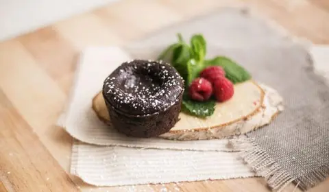 Mini fondant de chocolate espolvoreado con azúcar glas junto a frambuesas y hojas de menta sobre una rodaja de tronco