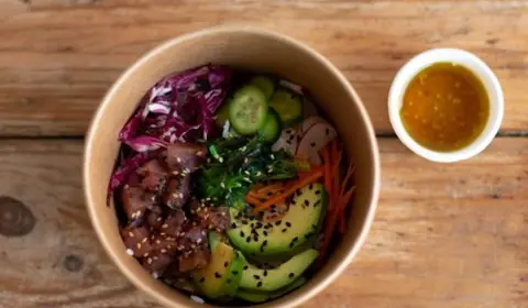Poke bowl en cuenco de cartón con atún marinado, aguacate, pepino, lombarda, wakame, zanahoria y sésamo, con salsa aparte