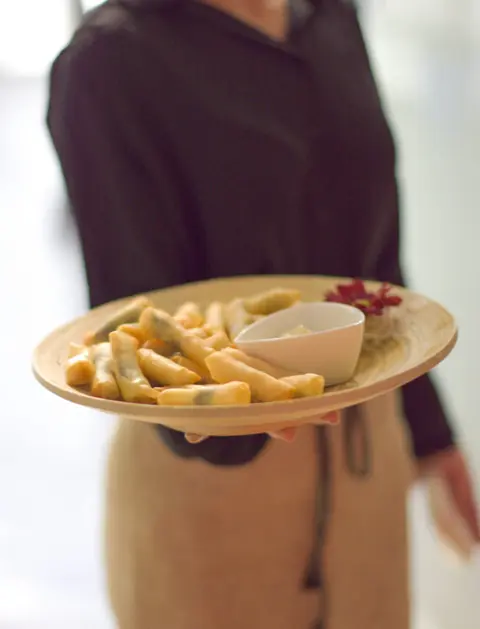Camarera con delantal ofreciendo un plato de mini rollitos de primavera con salsa durante un cóctel de catering