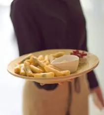 Camarera con delantal ofreciendo un plato de mini rollitos de primavera con salsa durante un cóctel de catering