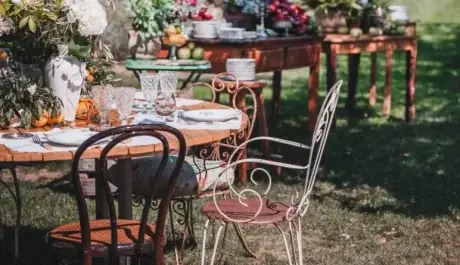 Mesa de boda al aire libre con sillas de forja, copas talladas y flores, con aparadores de madera sobre el césped