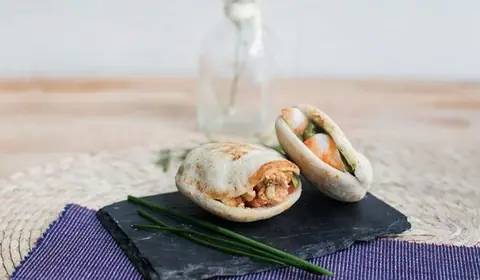Dos mini pitas rellenas, una de carne con verduras y otra con langostinos, sobre pizarra y mantel morado