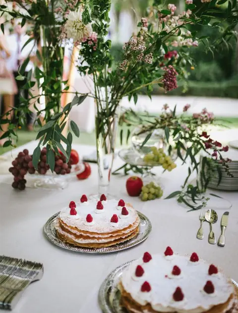Tartas de hojaldre con nata y frambuesas en bandejas de plata sobre una mesa de postres de boda al aire libre