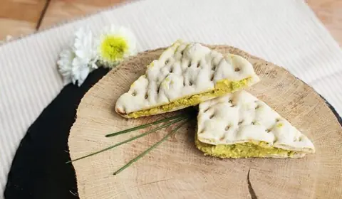 Dos triángulos de pan polar rellenos de una crema amarilla sobre una rodaja de tronco con cebollino y una margarita