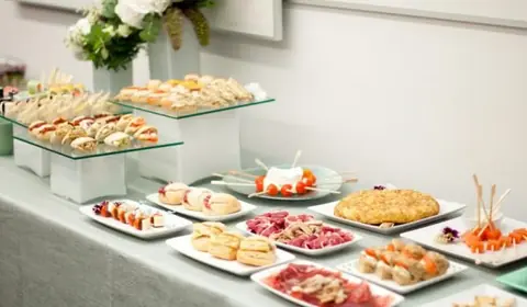 Bufé de picoteo con tortilla de patata, jamón, sándwiches, brochetas y mini bocadillos para eventos de empresa