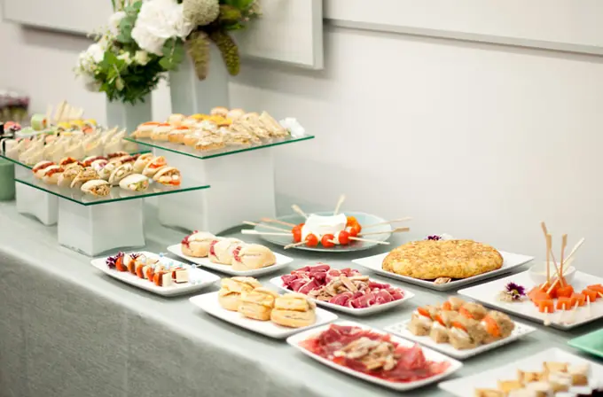 Bufé de comida de empresa con tortilla de patata, jamón, sándwiches, brochetas y mini bocadillos