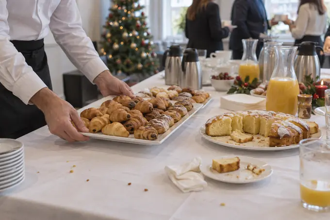 Camarero sirviendo un desayuno navideño de empresa con bollería, zumos y bizcocho casero en una oficina