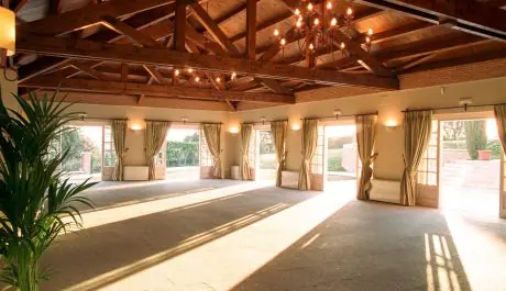 Salón para eventos con techo de vigas de madera, lámparas de araña y puertas acristaladas abiertas al jardín