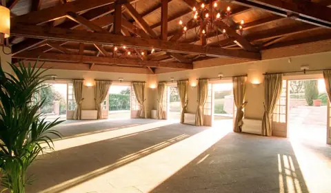 Salón para eventos con techo de vigas de madera, lámparas de araña y puertas acristaladas abiertas al jardín