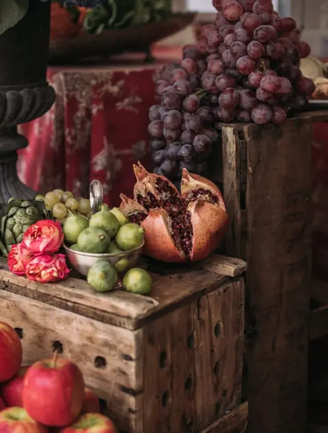 Bodegón de otoño con granadas, uvas, manzanas y rosas sobre cajas de madera en un evento de Cardamomo