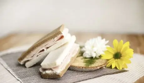 Sandwichitos de pan blanco y de centeno con fiambre y crema de queso, junto a una margarita amarilla