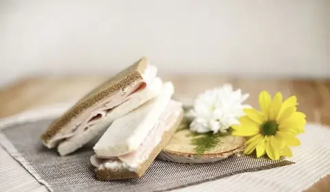 Sandwichitos de pan blanco y de centeno con fiambre y crema de queso, junto a una margarita amarilla