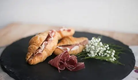 Mini croissants rellenos de jamón ibérico sobre pizarra redonda con un rizo de jamón y un ramillete de paniculata