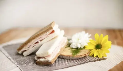 Sándwiches de pan de molde blanco y de centeno rellenos de jamón cocido y queso crema junto a margaritas
