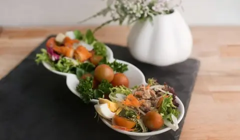 Tres cuencos blancos unidos con ensaladas de lechugas variadas, tomates cherry, huevo cocido, atún y otros ingredientes