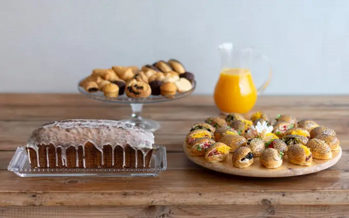 Desayuno de empresa con bizcocho glaseado, mini bollería, jarra de zumo de naranja y mini brioches de amapola