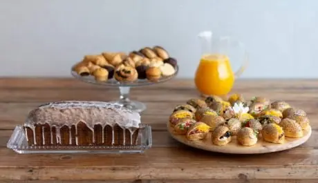 Desayuno de catering con bizcocho glaseado, mini bollería, jarra de zumo de naranja y mini brioche de amapola